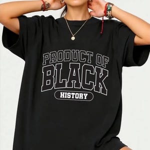May include: Black t-shirt with the text "PRODUCT OF BLACK HISTORY" in a white, collegiate-style font. The shirt has short sleeves and a relaxed fit, suitable for casual wear. The design is centered on the front of the shirt.