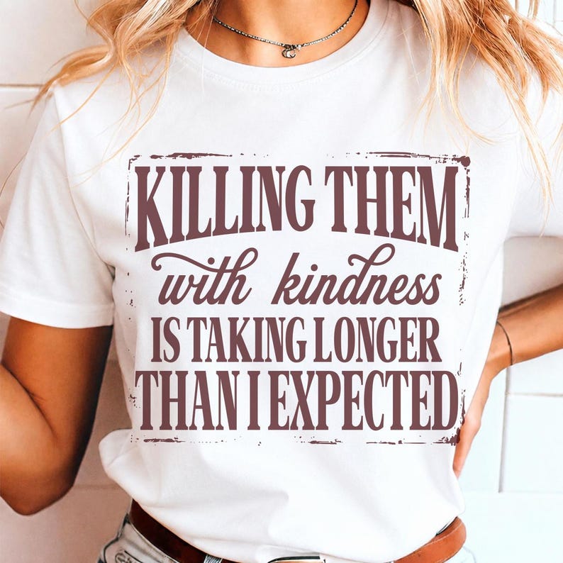 Puede incluir: Una camiseta blanca de manga corta con texto en marr&oacute;n oscuro que dice: "KILLING THEM with kindness IS TAKING LONGER THAN I EXPECTED." Las letras se presentan en una mezcla de fuentes en negrita y cursiva, encerradas en un borde rectangular desgastado.