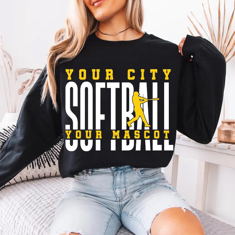 May include: Black sweatshirt with the text "YOUR CITY SOFTBALL YOUR MASCOT" in white and yellow block letters. A yellow softball player graphic is in the center. The sweatshirt is long-sleeved.
