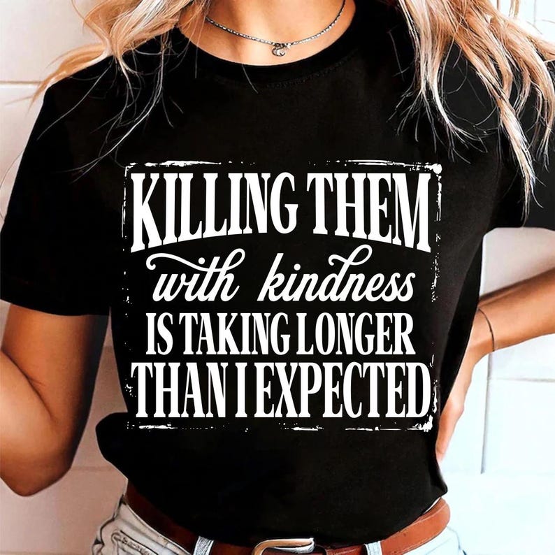 Puede incluir: Una camiseta negra de manga corta con texto blanco que dice: KILLING THEM with kindness IS TAKING LONGER THAN I EXPECTED. El dise&ntilde;o est&aacute; centrado en el pecho y utiliza una mezcla de fuentes en negrita, desgastadas y manuscritas.