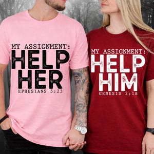 May include: Two matching t-shirts, one pink and one burgundy, with the text "MY ASSIGNMENT: HELP HER" and "MY ASSIGNMENT: HELP HIM" in large, bold letters. The pink shirt has "Ephesians 5:23" and the burgundy shirt has "Genesis 2:18" printed below the text.