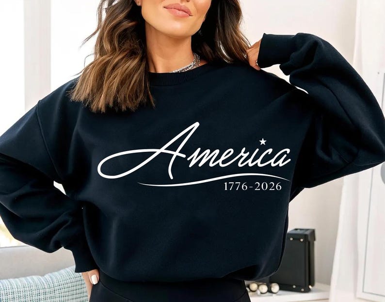 May include: A black sweatshirt with the word "America" in white script, a star, and the dates 1776-2026. The sweatshirt is a crew neck style.