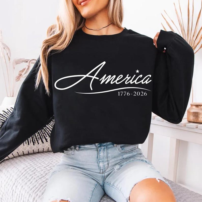 May include: Black crew neck sweatshirt with the word "America" in white script, a star, and the dates "1776-2026". The sweatshirt is a long-sleeved top.