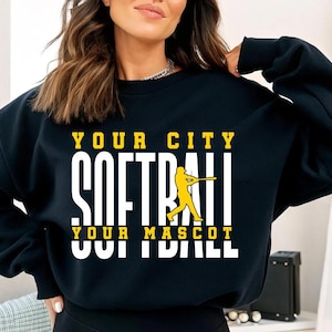 May include: Black sweatshirt with the text "YOUR CITY SOFTBALL YOUR MASCOT SOFTBALL" in white and yellow. A yellow softball player graphic is in the center. The sweatshirt is a casual style.