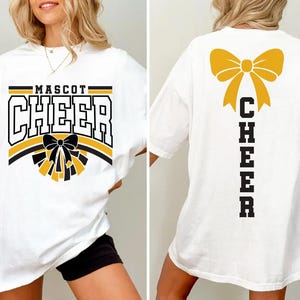 May include: White t-shirt with "MASCOT CHEER" in black, yellow, and white block letters. A black bow and yellow pom-poms are below the text. The back of the shirt has a yellow bow and the word "CHEER" in black.