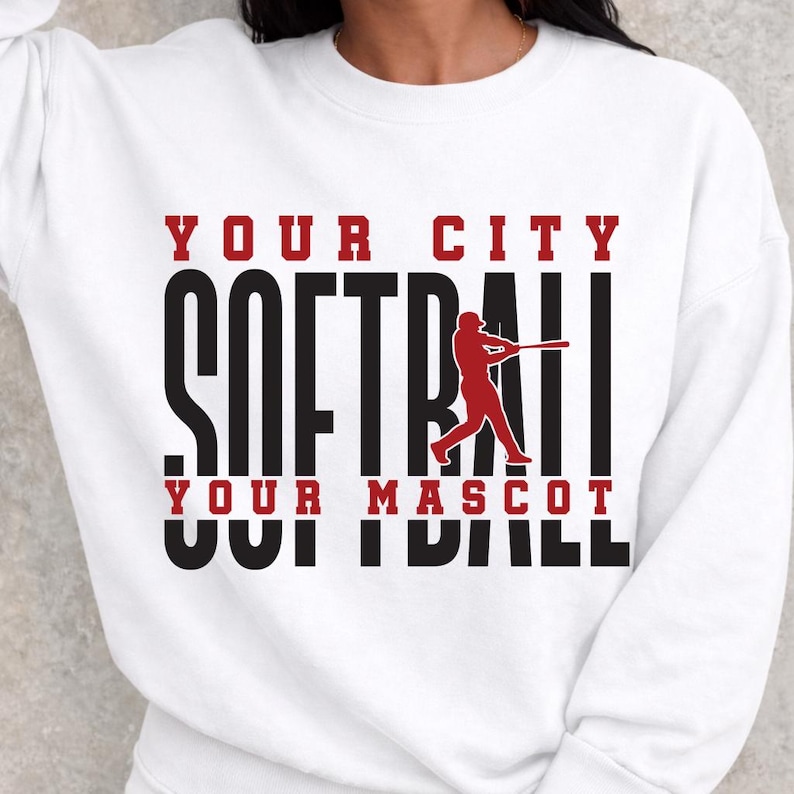 May include: White sweatshirt with the words "YOUR CITY SOFTBALL YOUR MASCOT" in black and red lettering. A red softball player silhouette is in the center. The sweatshirt is a crew neck style.