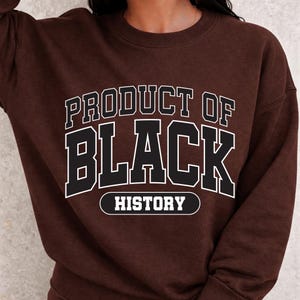 May include: A brown sweatshirt with the text "PRODUCT OF BLACK HISTORY" in white, outlined in black. The text is in a bold, collegiate-style font. The sweatshirt is a solid, dark brown color.