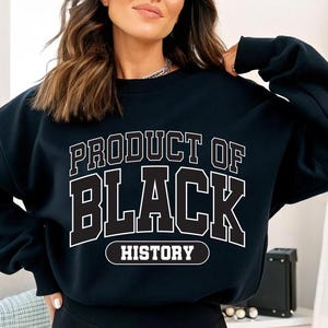 May include: Black sweatshirt with the text "PRODUCT OF BLACK HISTORY" in white block letters. The sweatshirt is a crew neck style and appears to be made of a soft material. The text is outlined in black.