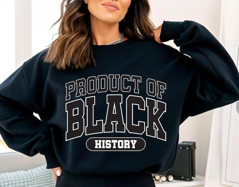 May include: Black sweatshirt with the text "PRODUCT OF BLACK HISTORY" in white block letters. The sweatshirt is a crew neck style and appears to be made of a soft material. The text is outlined in black.
