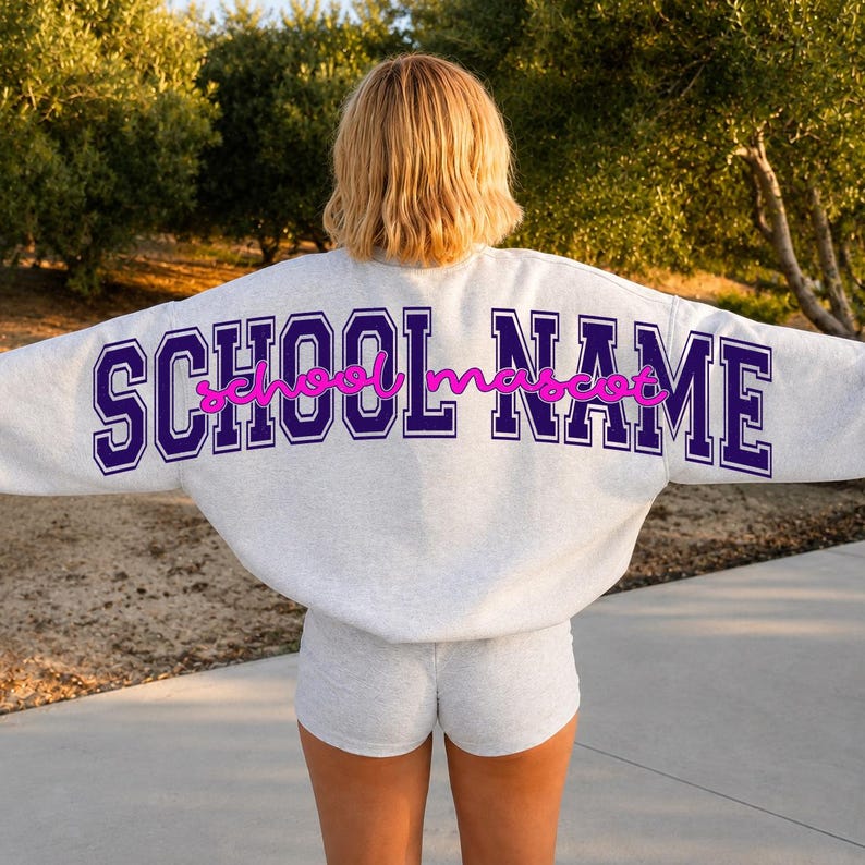 May include: A light gray crewneck sweatshirt and matching shorts set. The back of the sweatshirt features the text SCHOOL NAME in large, dark purple block letters with the word school mascot written in a pink cursive script across the center.