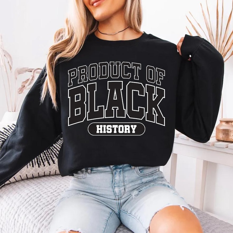May include: Black sweatshirt with the text "PRODUCT OF BLACK HISTORY" in white block letters. The sweatshirt is long-sleeved and has a crew neck. The text is outlined in white.