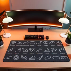 May include: A black desk mat featuring white outlines of various race tracks. The mat is placed on a light wood desk, with a curved monitor, keyboard, mouse, and two desk lamps. The text "CYBERNETIC CITY TRACK" is visible.