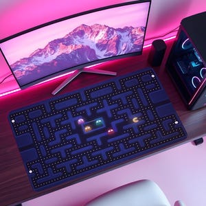 May include: A computer desk setup featuring a curved monitor displaying a mountain scene, a black computer tower, and a blue Pac-Man themed mousepad. The mousepad has a maze design with Pac-Man and ghost characters.