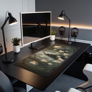 May include: A black desk with a large computer monitor, two black desk lamps, and a decorative mousepad. The mousepad features a forest scene with a dark figure and glowing butterflies. Two pairs of headphones and small potted plants are also on the desk.