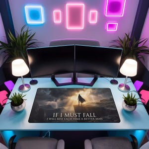 May include: A modern gaming desk setup featuring two black computer monitors, a mousepad with a dramatic landscape and text, two small lamps, and potted plants. The mousepad reads "IF I MUST FALL, I WILL RISE EACH TIME A BETTER MAN."