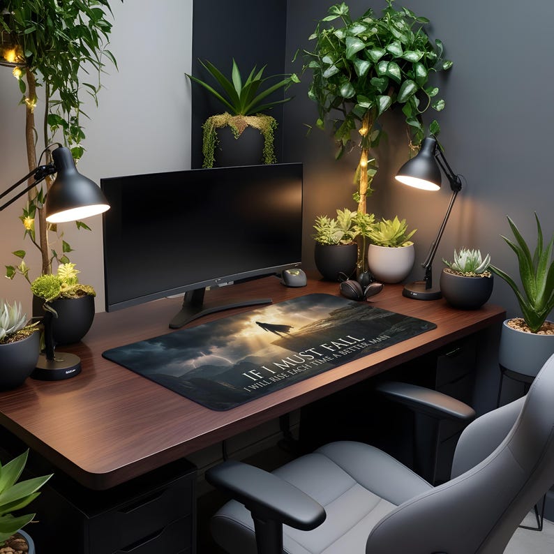 May include: A home office setup with a dark wood desk, a computer monitor, and a mousepad featuring a wolf silhouette and the text "IF I MUST FALL I WILL RISE EACH TIME A BETTER MAN." The desk is surrounded by plants and black desk lamps.