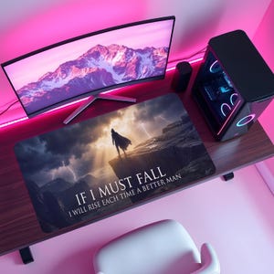 May include: A rectangular mousepad with a dramatic landscape featuring a figure on a cliff under a stormy sky. The text "IF I MUST FALL, I WILL RISE EACH TIME A BETTER MAN" is printed on the pad. The pad is on a wooden desk with a computer monitor and tower.