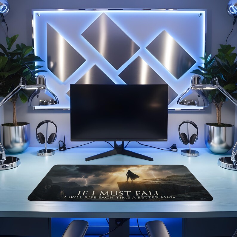 May include: Black rectangular desk mat with a dramatic landscape featuring a figure on a cliff under a stormy sky with lightning. The mat has the text "IF I MUST FALL I WILL RISE EACH TIME A BETTER MAN."