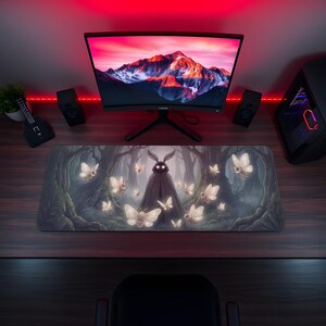 May include: A large rectangular mousepad featuring a fantasy forest scene with a dark figure and glowing moths. The mousepad is on a wooden desk, with a computer monitor, speakers, and a PC tower in the background.