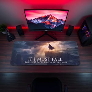 May include: A rectangular mouse mat featuring a dramatic landscape scene with a figure on a cliff, and the text "IF I MUST FALL I WILL RISE EACH TIME A BETTER MAN." The scene includes mountains, lightning, and a sunset.