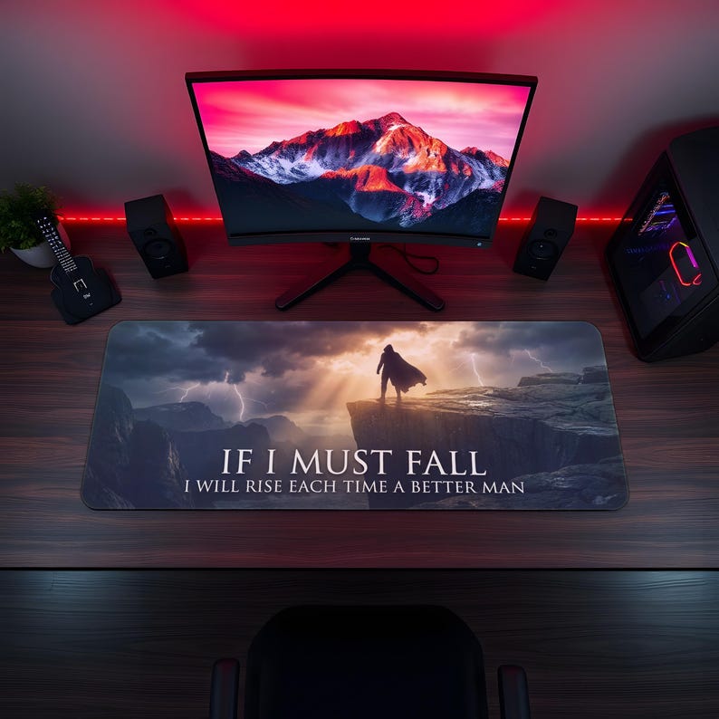 May include: A rectangular mouse mat featuring a dramatic landscape scene with a figure on a cliff, and the text "IF I MUST FALL I WILL RISE EACH TIME A BETTER MAN." The scene includes mountains, lightning, and a sunset.