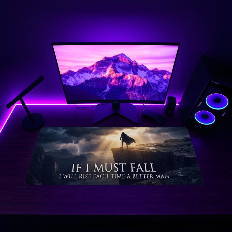 May include: A rectangular mousepad with a dramatic landscape featuring a figure on a cliff under a stormy sky. The mousepad has the text "IF I MUST FALL I WILL RISE EACH TIME A BETTER MAN". The background includes a computer monitor and components, all illuminated with purple light.