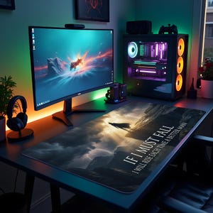 May include: A gaming desk setup with a large monitor, a desktop computer, and a mousepad. The mousepad features a dramatic landscape design with the text "IF I MUST FALL, I WILL RISE EACH TIME A BETTER MAN."