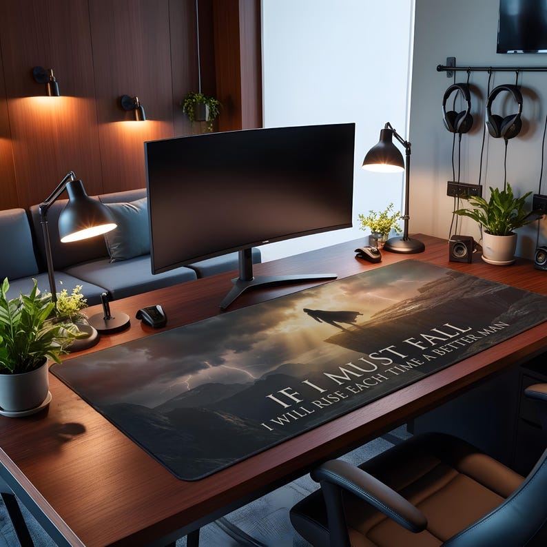 May include: A large rectangular desk mat with a dramatic landscape design, a silhouetted figure, and the text "IF I MUST FALL I WILL RISE EACH TIME A BETTER MAN." The mat is black with a sunset design.