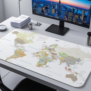 May include: A rectangular desk mat featuring a world map design with continents and oceans labeled in various colors. The mat is placed on a white desk, with a computer monitor, clock, and other office supplies visible in the background.