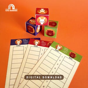 Può includere: Un set di cubi di gioco colorati e schede segnapunti. I cubi presentano illustrazioni di conigli e orsi su ogni lato. Le schede segnapunti sono etichettate con "Bunny" e "Bear" e il testo "Digital Download". Lo sfondo è arancione.