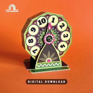 Peut inclure: Une roue artisanale en papier avec les chiffres 1 à 10, sur fond orange. La roue présente un motif vert et jaune avec un élément décoratif central. La base est noire et verte. Le texte "TÉLÉCHARGEMENT NUMÉRIQUE" est en bas.