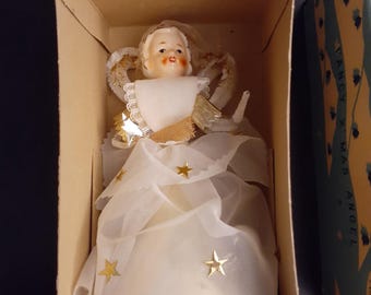 May include: A vintage angel tree topper figurine with a painted face, wearing a white sheer gown adorned with gold star accents, white lace trim, and gold metallic fabric details, presented inside a cardboard box labeled FANCY X'MAS ANGEL.