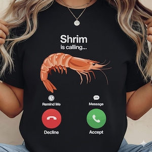 May include: Black t-shirt with a graphic of a cooked shrimp and the words "Shrimp is calling...". Below the shrimp are the words "Remind Me", "Decline", "Message", and "Accept" with corresponding icons.