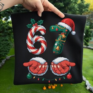 May include: Black Christmas-themed pillow with the number 67. The number 6 is designed as a red and white candy cane, and the number 7 is green with a Santa hat. Santa's hands are at the bottom, holding ornaments.