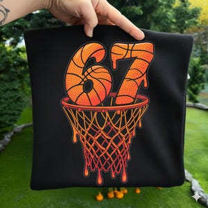 May include: Black pillow with a basketball-themed design. The design features the number 67 in orange, with a basketball texture, above a basketball net. The net and the numbers have a dripping effect.
