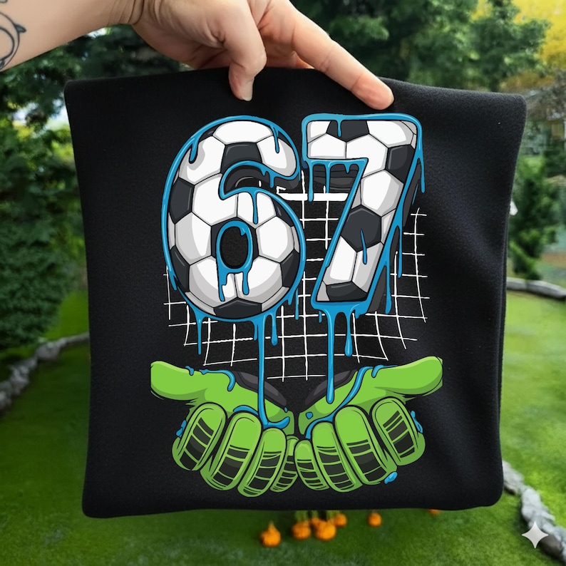 May include: Black square pillow with a soccer-themed design. The number "67" is depicted with a soccer ball pattern and blue dripping accents. Green goalie gloves are at the bottom.