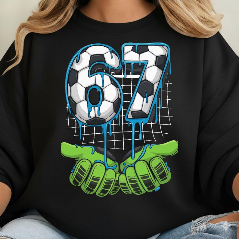 May include: Black sweatshirt with a soccer-themed graphic. The number "67" is designed with a soccer ball pattern and blue dripping accents. Below, green goalie gloves appear to be catching the number. A grid pattern is in the background.