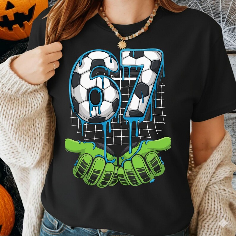 May include: Black t-shirt featuring the number "67" in a soccer ball design with blue dripping accents. The number is set against a white grid, with green hands at the bottom.