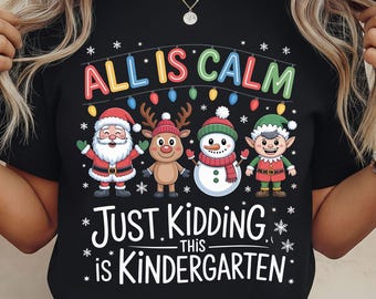 Könnte beinhalten: Schwarzes T-Shirt mit einem farbenfrohen Motiv von Weihnachtsmann, Rentier, Schneemann und Elf. Der Text lautet "ALL IS CALM" und "JUST KIDDING...THIS IS KINDERGARTEN", mit Schneeflocken-Akzenten.