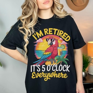 May include: Black t-shirt with a colorful graphic of a parrot wearing sunglasses, holding a drink, and the text "I'M RETIRED IT'S 5 O'CLOCK EVERYWHERE". The parrot is perched on a palm tree branch with a sunset background.