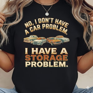 May include: Black t-shirt with the text "NO, I DON'T HAVE A CAR PROBLEM. I HAVE A STORAGE PROBLEM." Four vintage cars are illustrated above the text. The text and car illustrations are in shades of yellow, orange, and white.