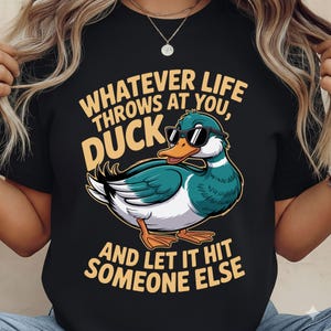 May include: Black t-shirt with a cartoon duck wearing sunglasses. The shirt features the text "WHATEVER LIFE THROWS AT YOU, DUCK, AND LET IT HIT SOMEONE ELSE" in yellow and white.