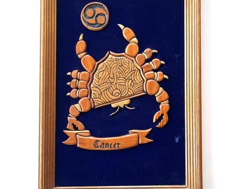 May include: Wooden framed artwork featuring a detailed crab design, the Cancer zodiac symbol, and a banner with the word "Cancer." The crab is intricately carved with a light brown finish, set against a dark blue background. The frame is a warm, golden brown.