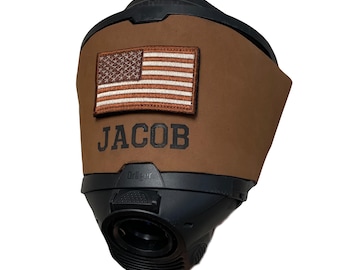 May include: A black Dräger respirator mask featuring a brown leather cover. The cover displays a rectangular embroidered American flag patch and the name JACOB printed in bold black capital letters centered below the flag on the leather surface.