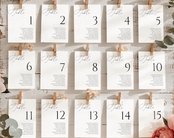 May include: A white wooden board displaying fifteen rectangular table seating cards, each secured with a small wooden clip. The cards feature the word Table followed by a number from 1 to 15, with a list of names printed in black ink below.