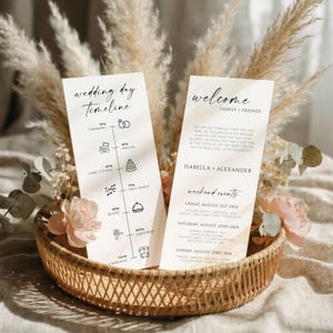 Pode incluir: Duas cartões de cronograma do dia do casamento e um cartão de boas-vindas em uma cesta de vime. O cartão de cronograma inclui cerimônia, fotos, corte do bolo, primeira dança, buffet, fogos de artifício e carruagens. O cartão de boas-vindas inclui os nomes Isabella + Alexander e eventos de fim de semana.