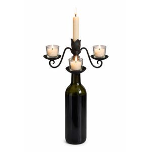 Puede incluir: Un candelabro de metal negro con tres candeleros pequeños y un candelero alto, sujeto a una botella de vino verde oscuro. Las velas están encendidas, sobre un fondo blanco.