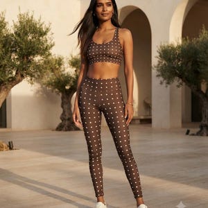 May include: A brown athletic set consisting of a scoop-neck sports bra and high-waisted leggings, both featuring a repeating pattern of small white polka dots. The outfit is paired with simple white sneakers, creating a coordinated look.