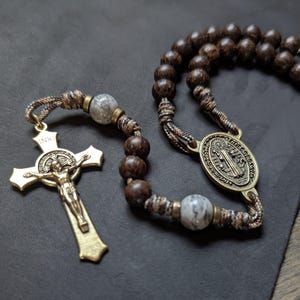 May include: A rosary with dark brown wooden beads and a gold-colored metal crucifix. The crucifix features the figure of Jesus Christ and the letters INRI. The rosary also includes a medal with a religious figure.