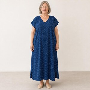 May include: A floor-length navy blue dress featuring a repeating pattern of small white circles. The garment has a V-neckline, short sleeves, and a straight silhouette with side slits at the hem, providing a simple and functional design.